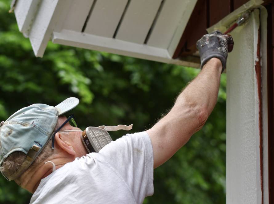 A man painting house exterior with white color